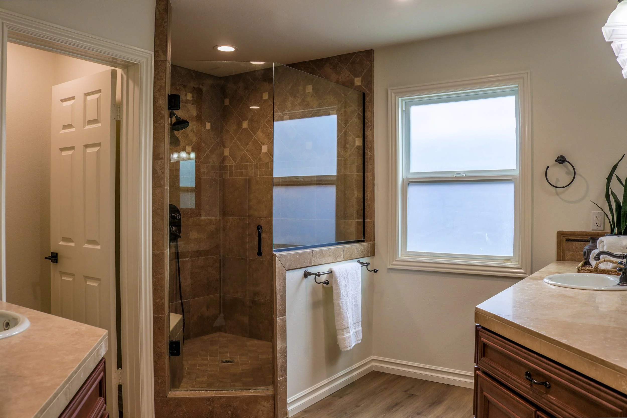 A bathroom with a glass-enclosed shower with brown tile and a window with frosted glass.