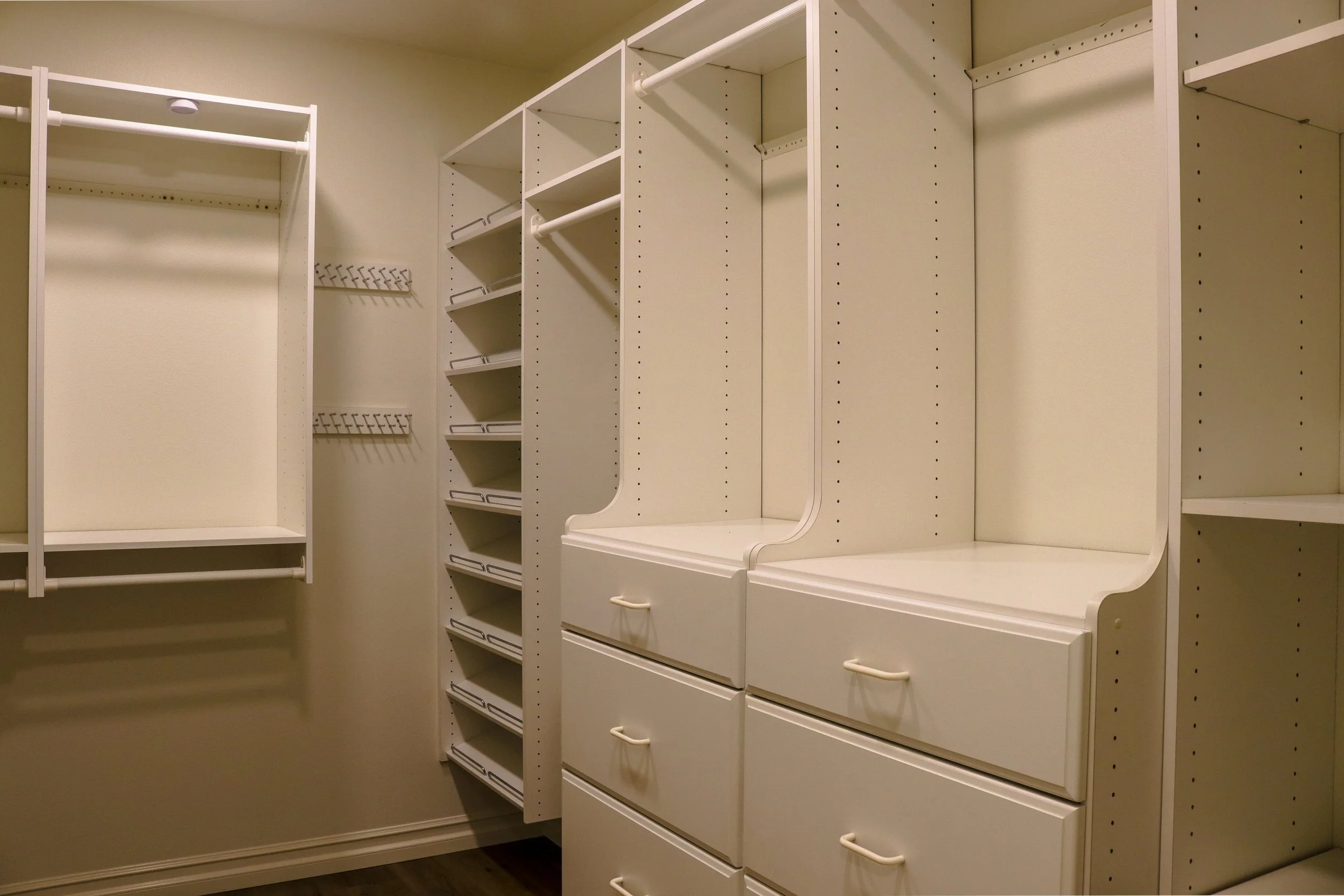 Empty white closet with shelves, drawers, and hanging rods inside a room.