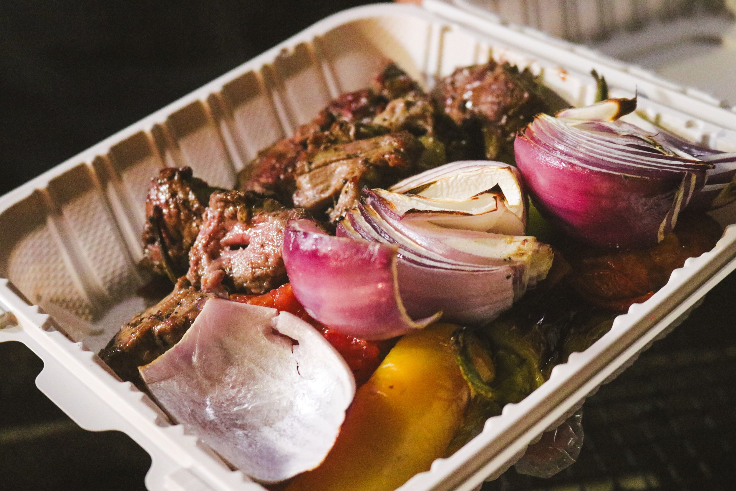 Grilled meat with roasted red onions in a white plastic takeout container