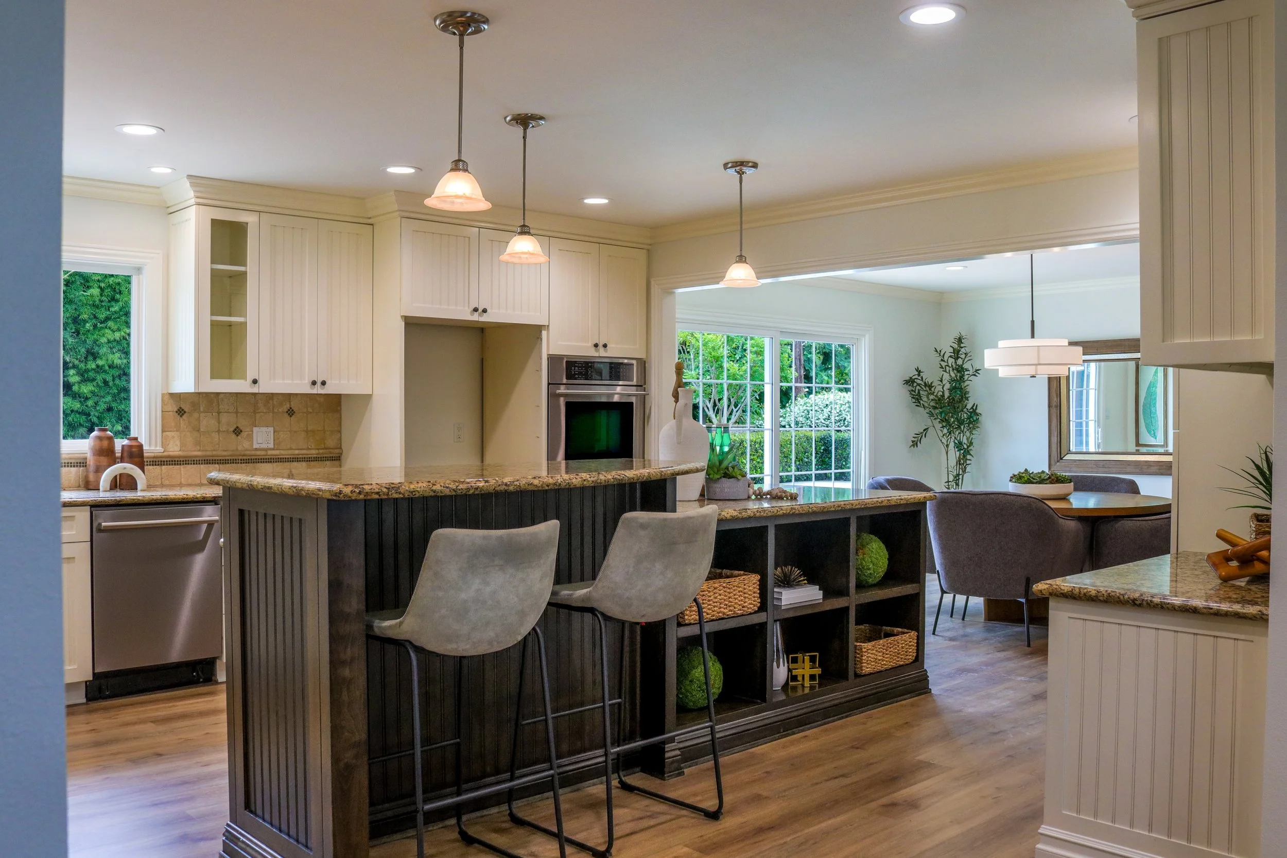 Open-concept kitchen and dining area with hanging pendant lights, white cabinetry, a granite countertop island, large windows, and dining chairs.