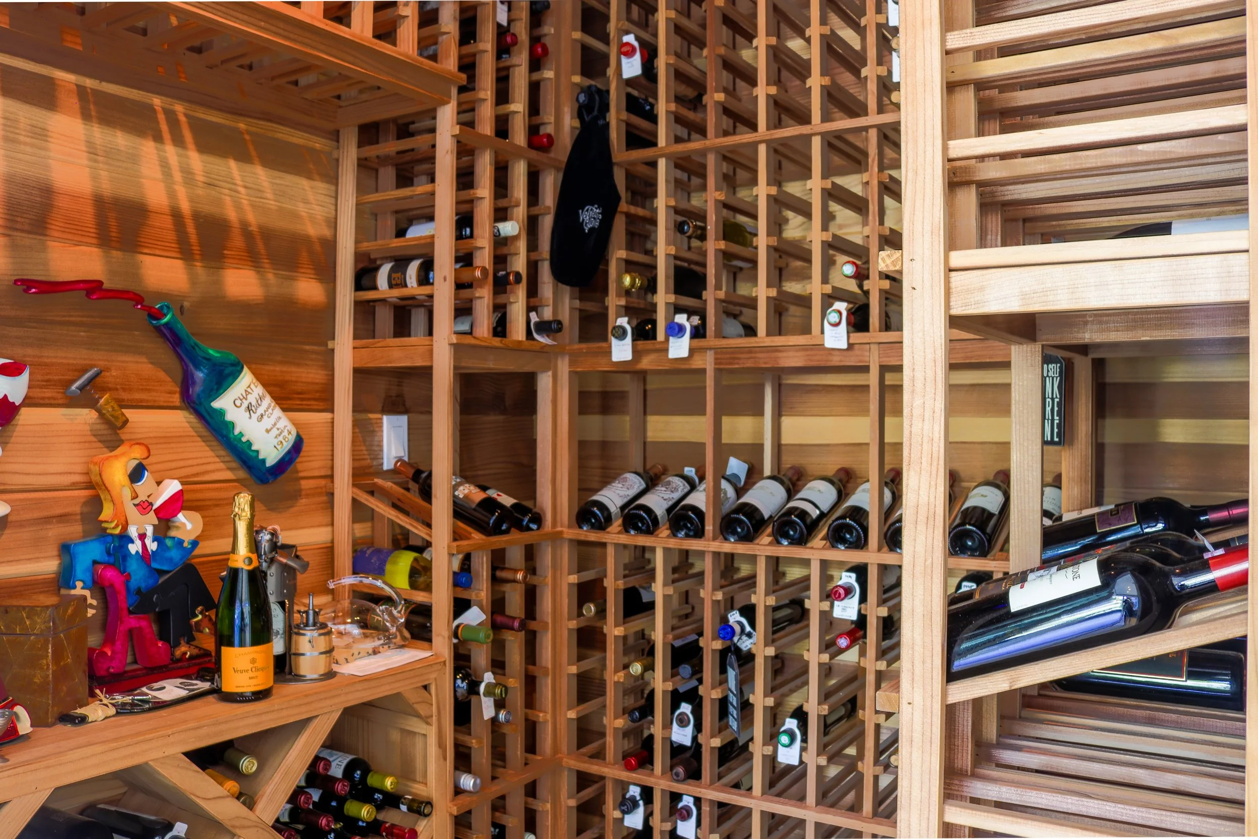A wooden wine rack filled with various bottles of wine, with a small table in front holding a champagne bottle, a small figurine, and miscellaneous items.