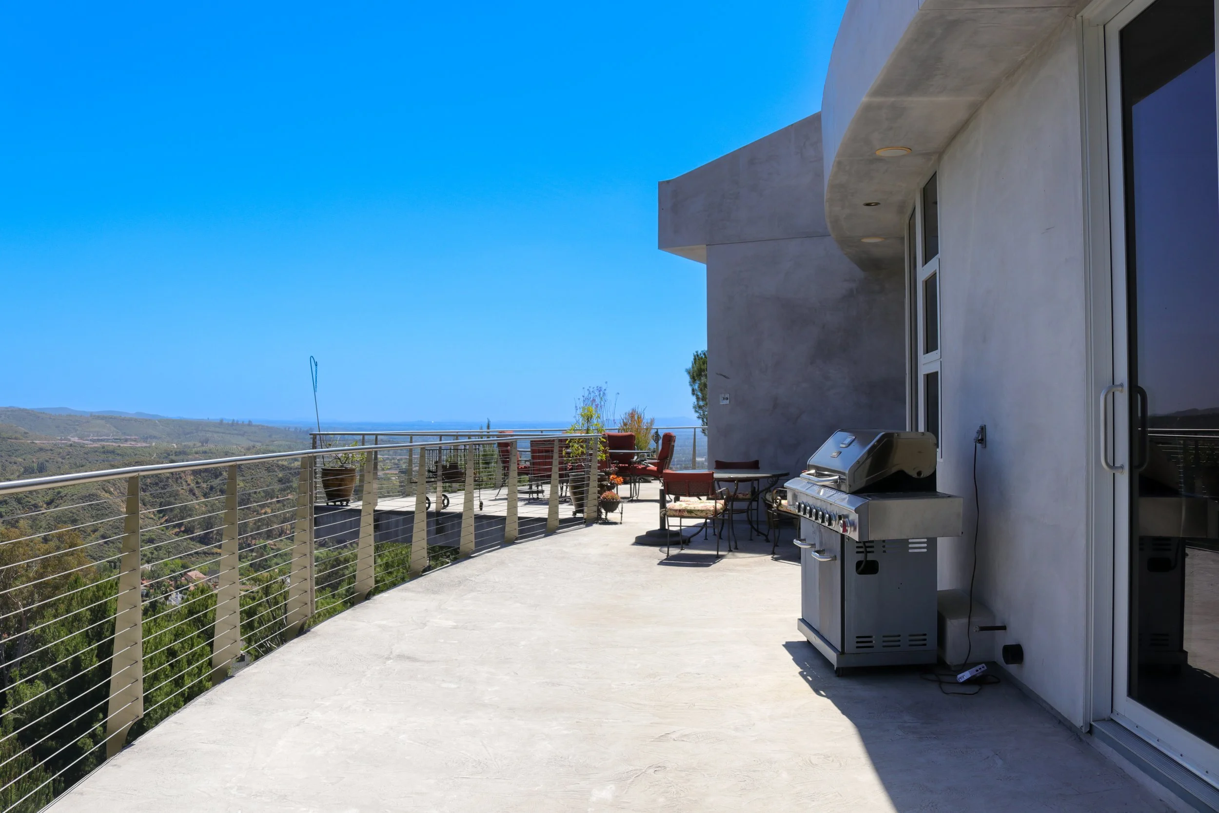 Balcony with outdoor furniture, a grill, and a view of rolling hills and a clear blue sky.