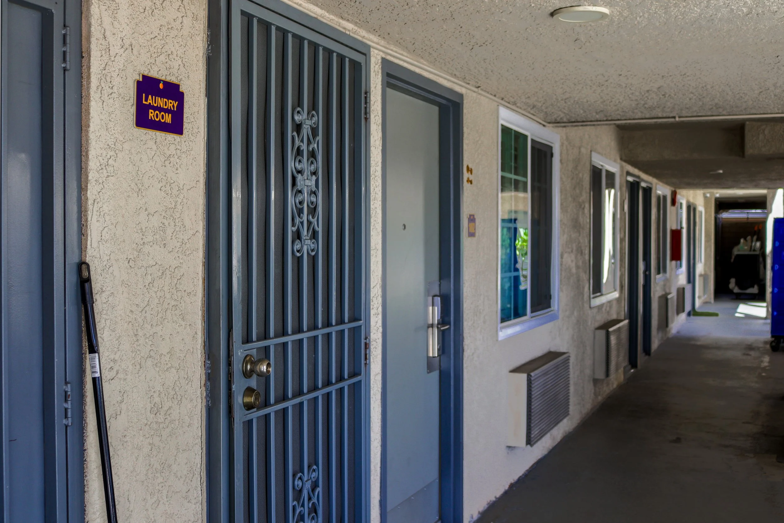 Apartment building corridor with blue doors, windows, and a sign that reads 'Laundry Room' on the wall.
