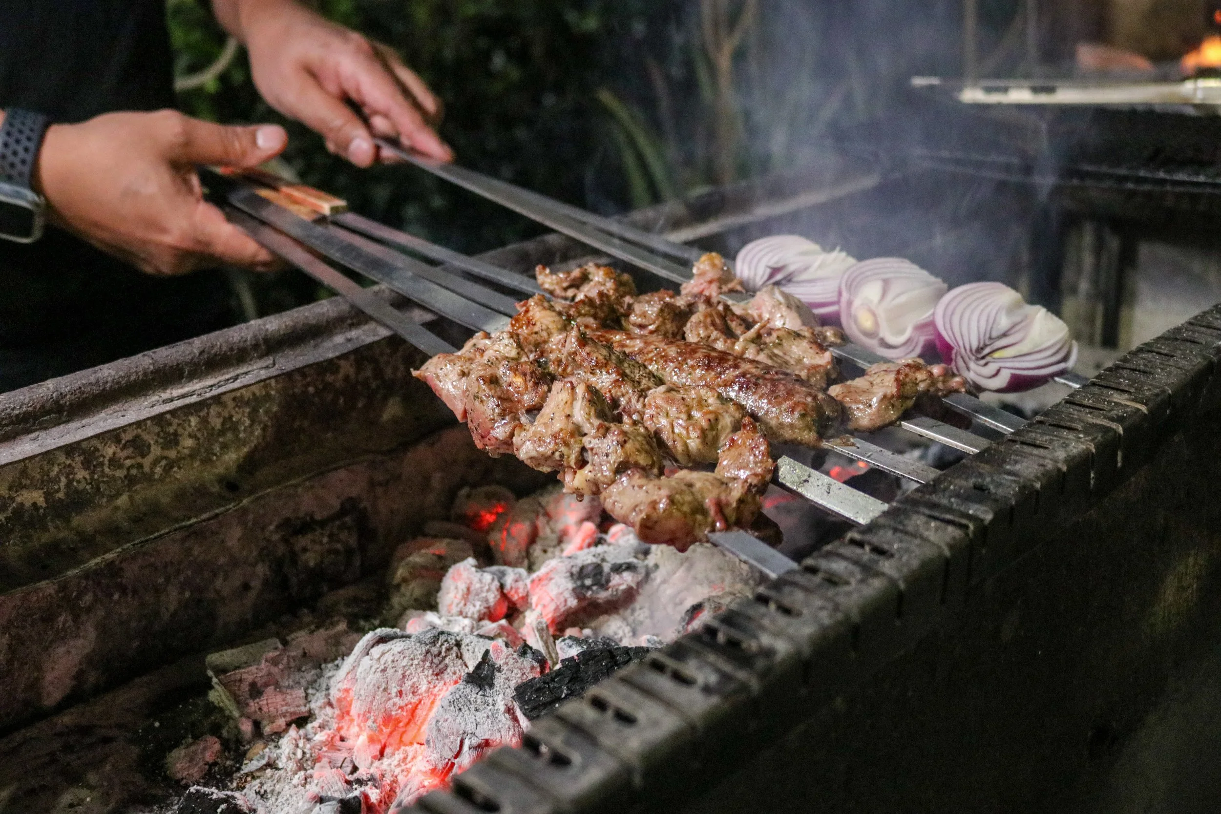 Meat and vegetables grilling on an outdoor barbecue over hot coals at night.
