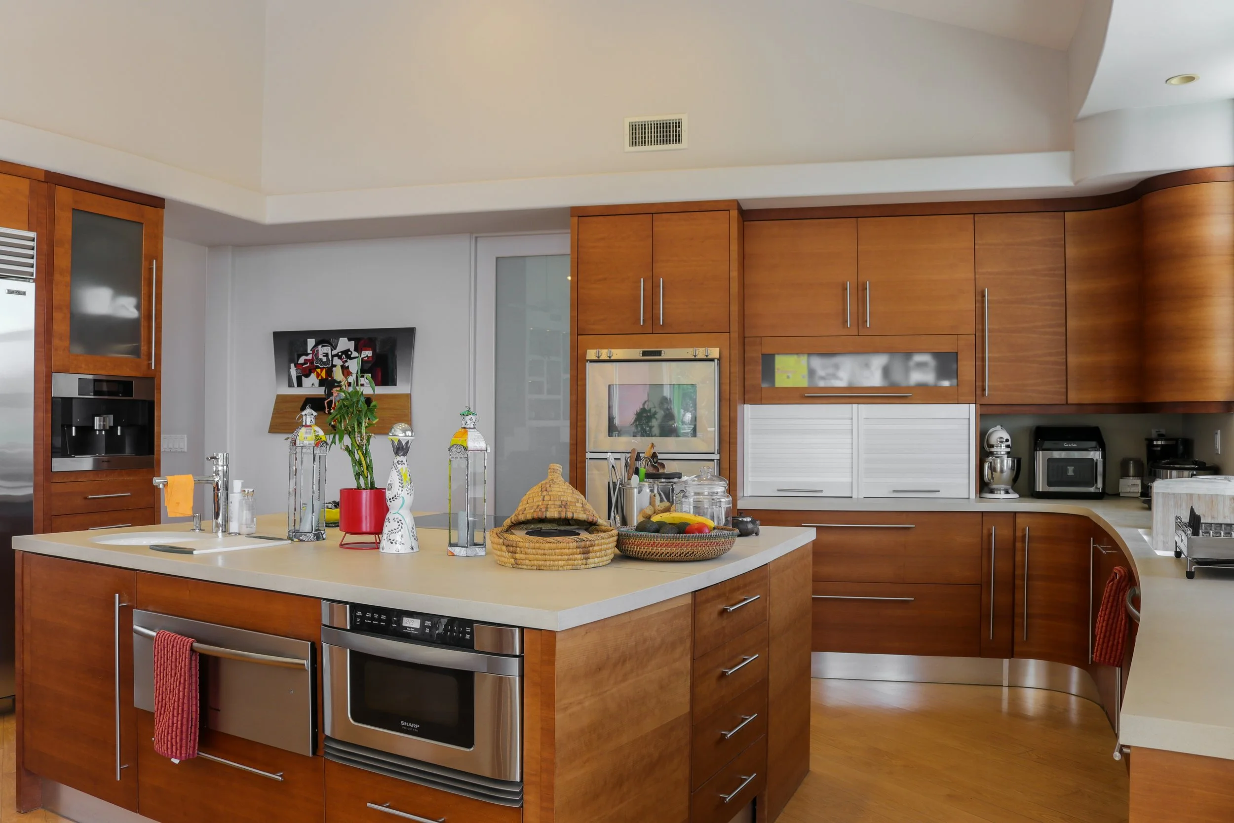 Modern kitchen with wooden cabinets, white countertops, stainless steel appliances, and a central island with decorative items and fruits.