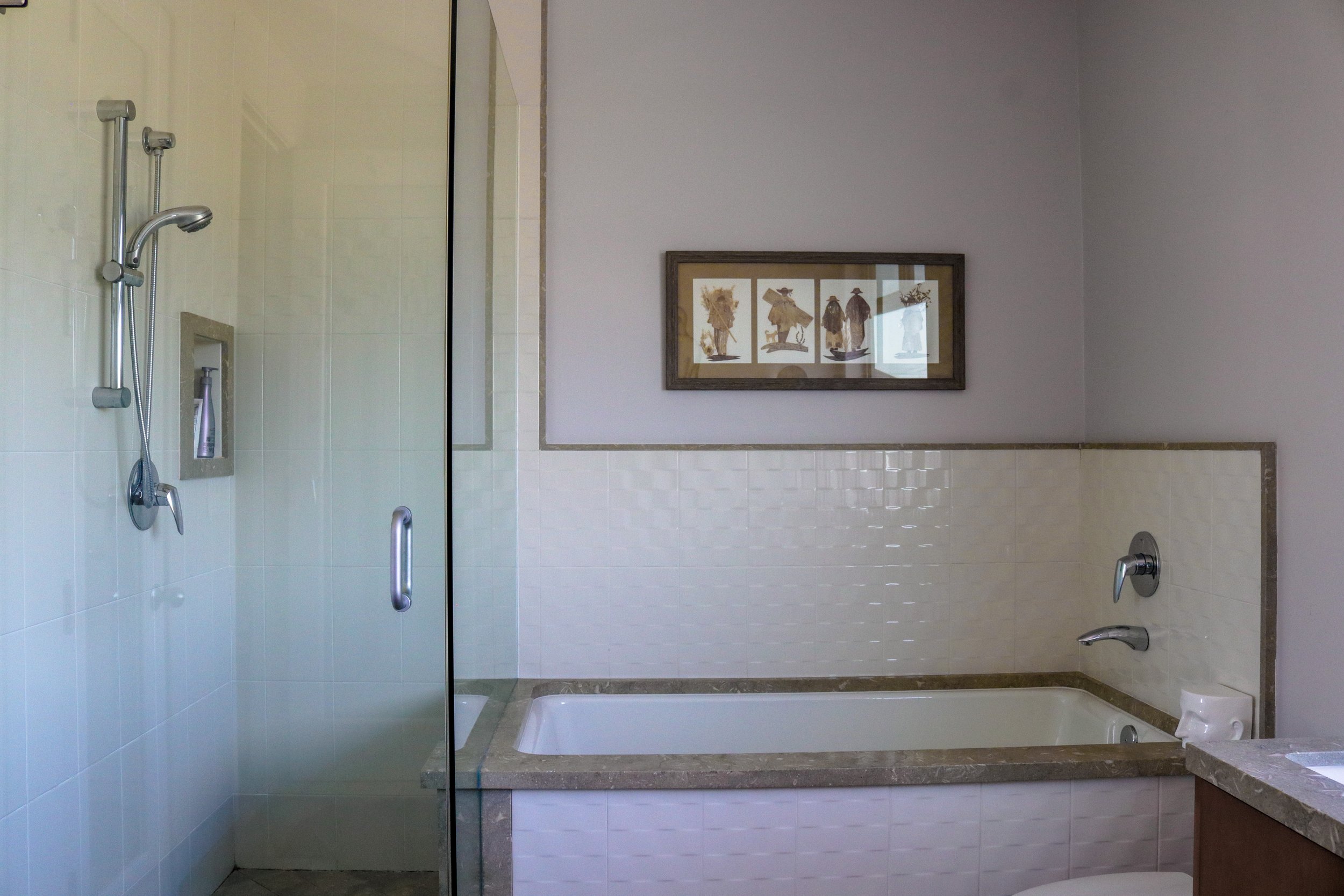 Bathroom with a walk-in shower, framed artwork on the wall, and a vanity with a marble countertop.
