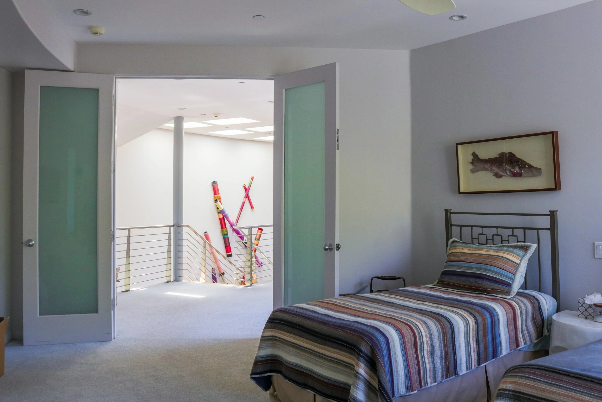 A bedroom with striped bedding on twin beds, a closet door open to an area with colorful rolled-up items, and a framed picture of a fish on the wall.
