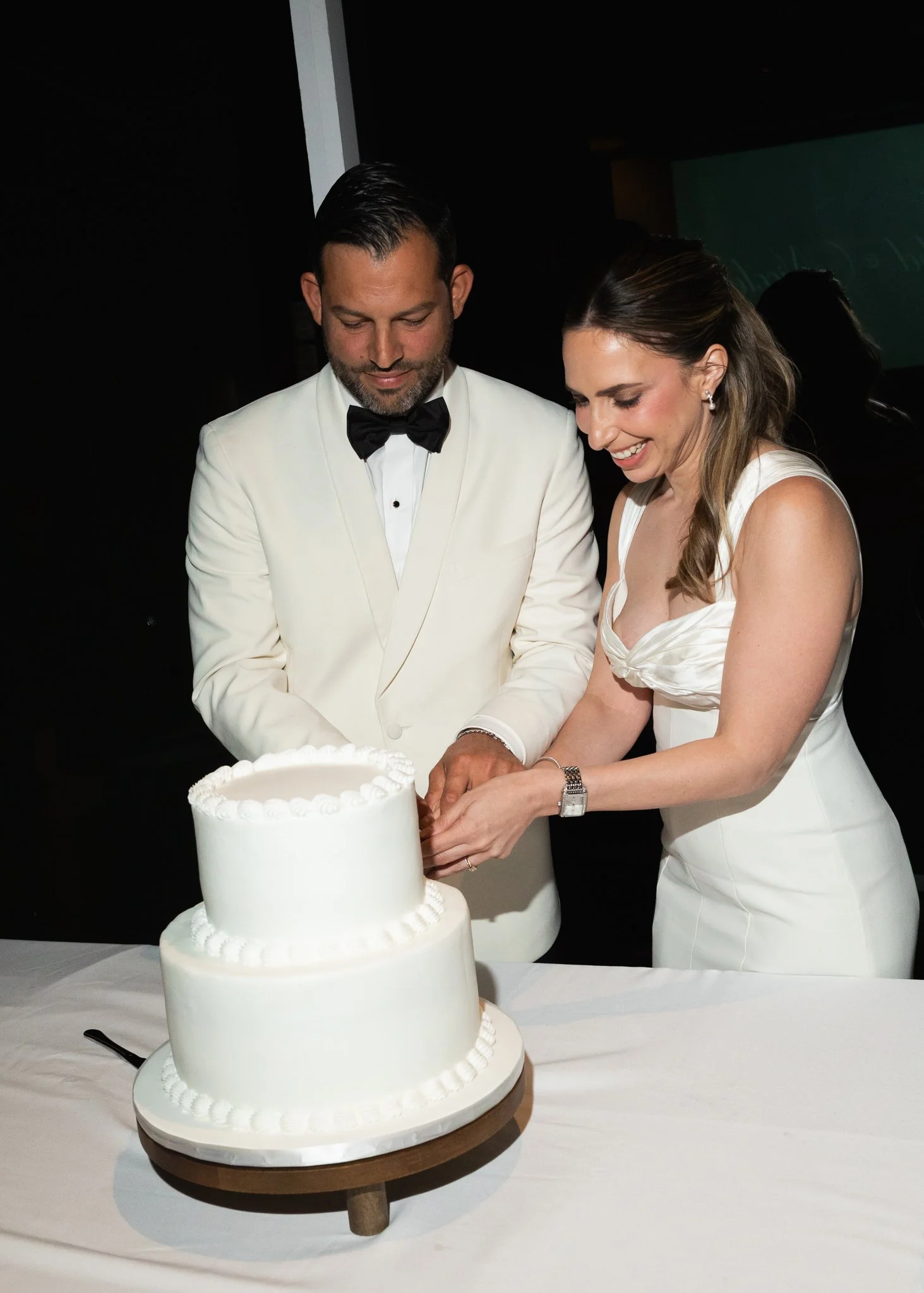 A bride and groom in wedding attire cutting a white wedding cake together at their wedding reception.