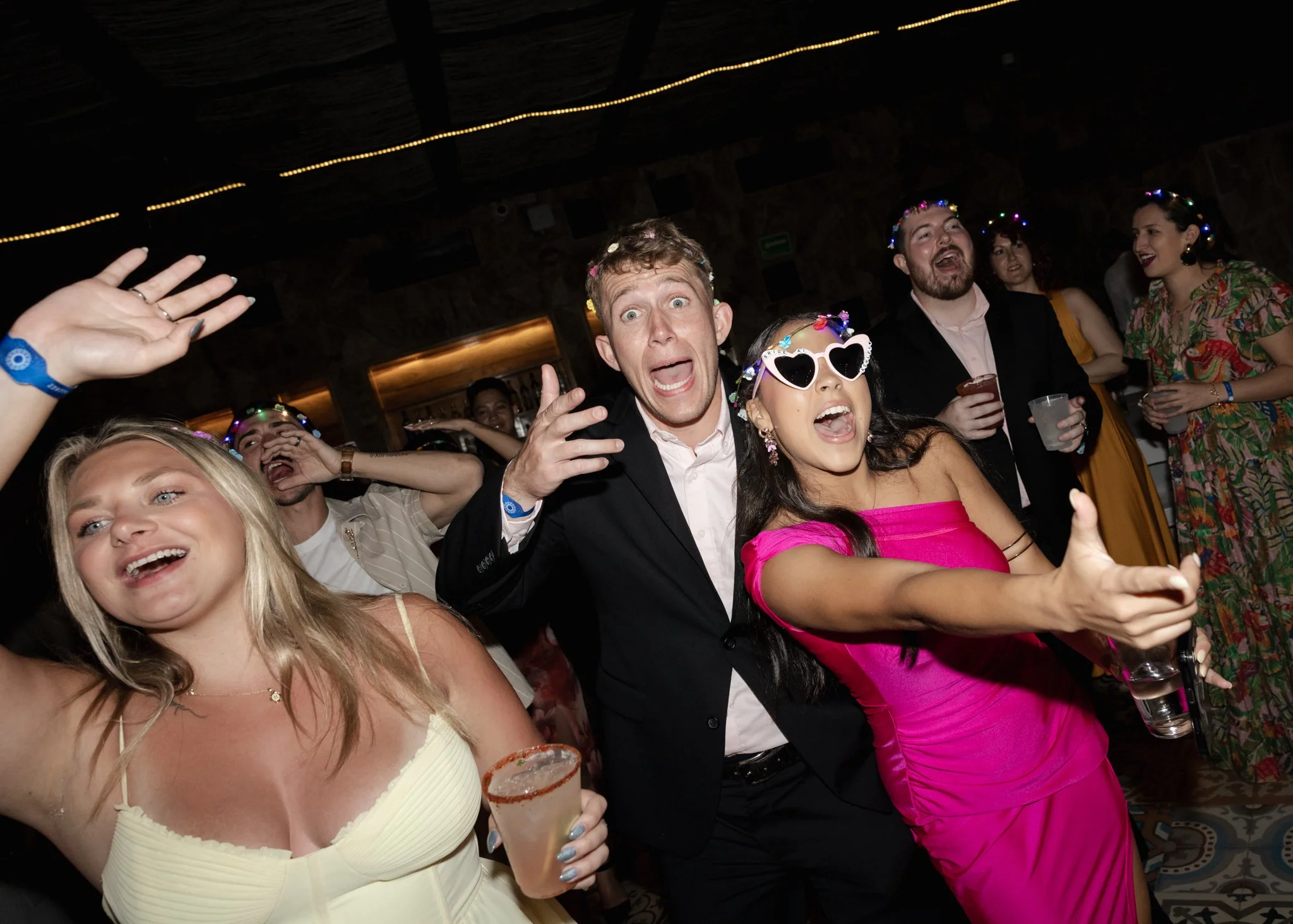 People celebrating at a party, wearing colorful accessories and stylish outfits, smiling, and holding drinks.