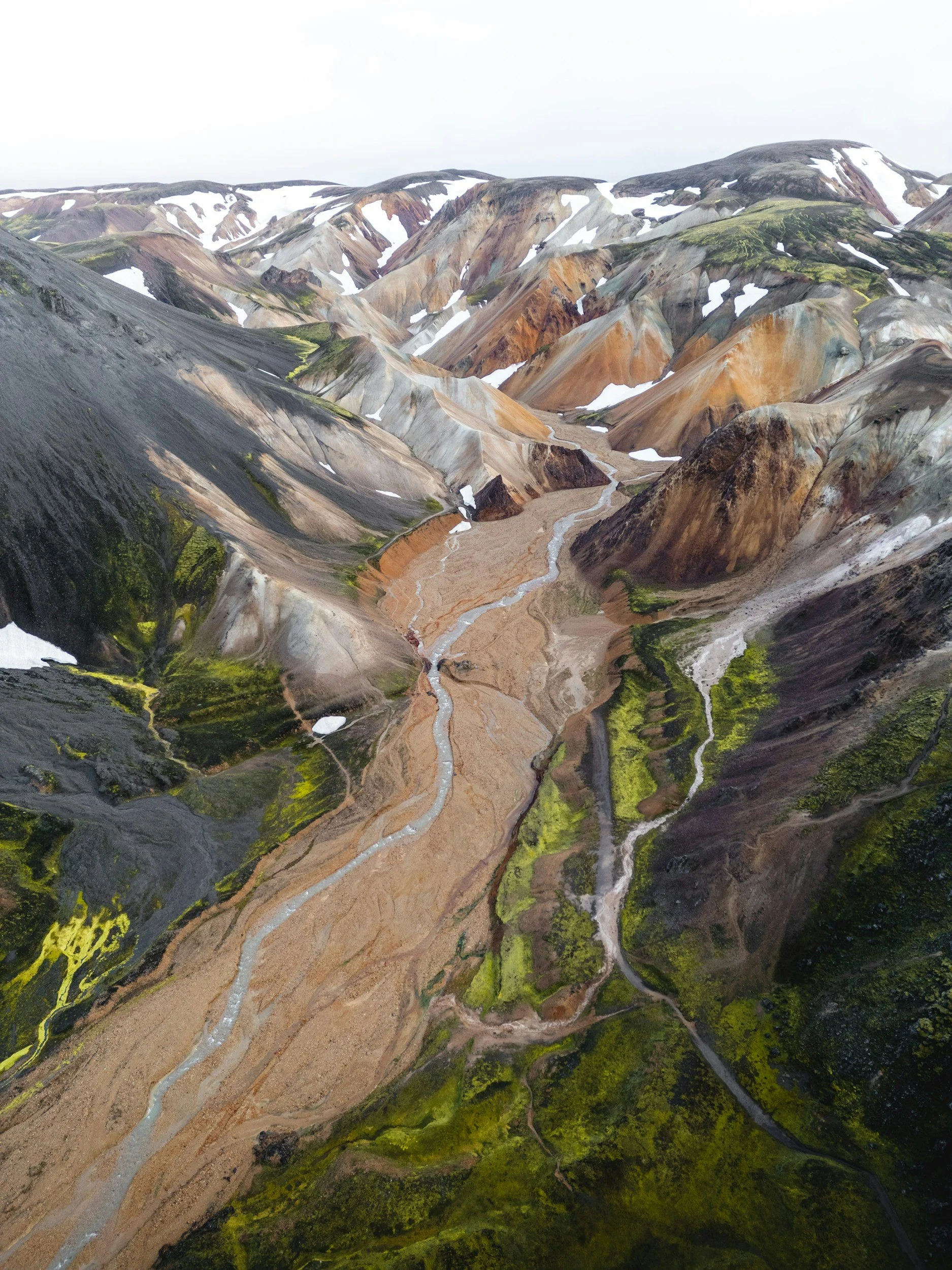Aerial view of a colorful, mountainous landscape with winding river and patches of snow.
