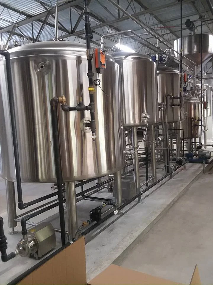 Industrial brewing or processing tanks made of stainless steel in a factory setting, connected by pipes and valves for manufacturing or processing liquids.