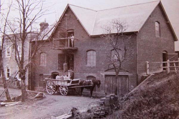 Old brick house with a horse-drawn wagon parked in front, leafless trees, and a dirt yard.