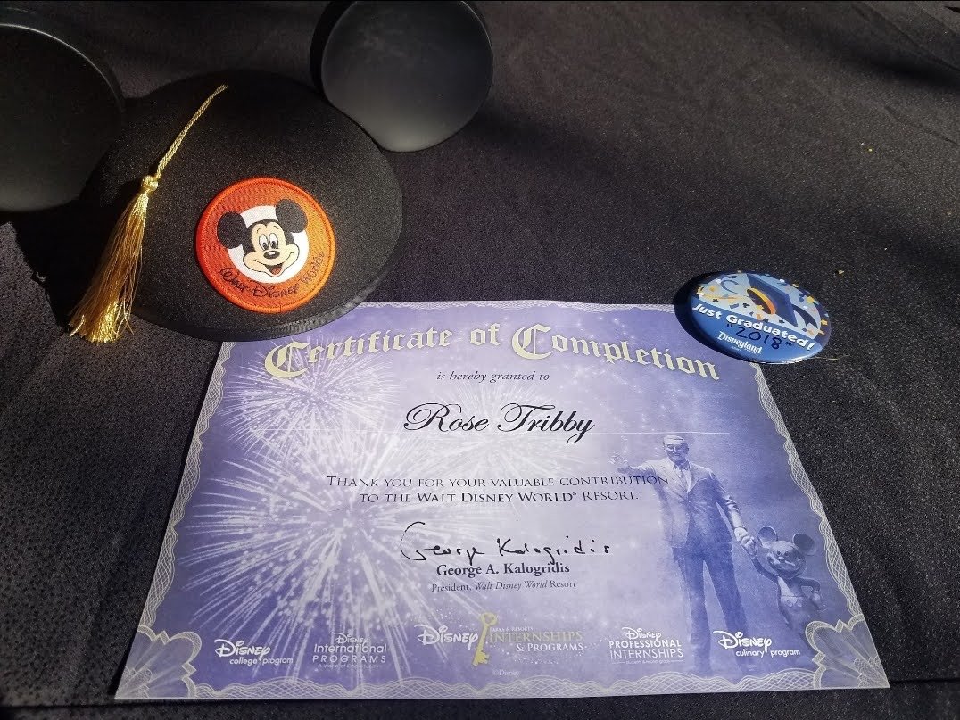 Disney graduation cap with Mickey Mouse patch, blue graduation badge, and certificate of completion from Walt Disney World Resort.
