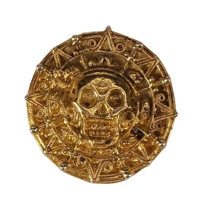 A gold decorative object with a skull in the center, surrounded by geometric patterns and star shapes