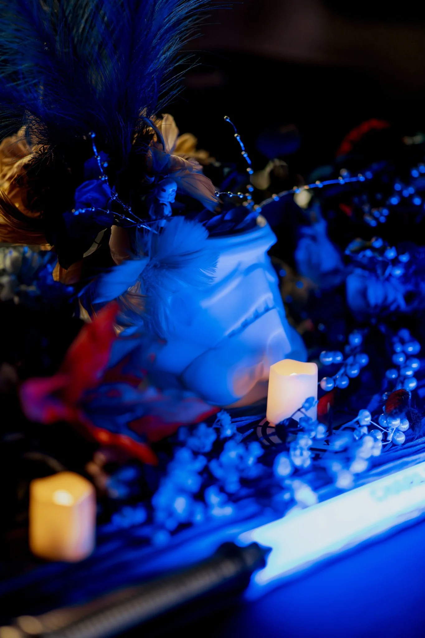 Close-up of a decorative, illuminated display featuring feathers, beads, string lights, and candles with a dark background.