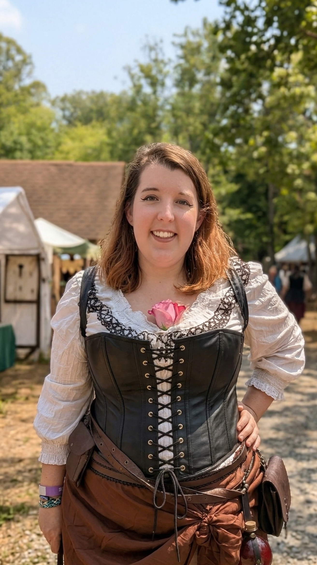 A woman dressed in medieval or fantasy-style costume at an outdoor event, with tents and trees in the background.