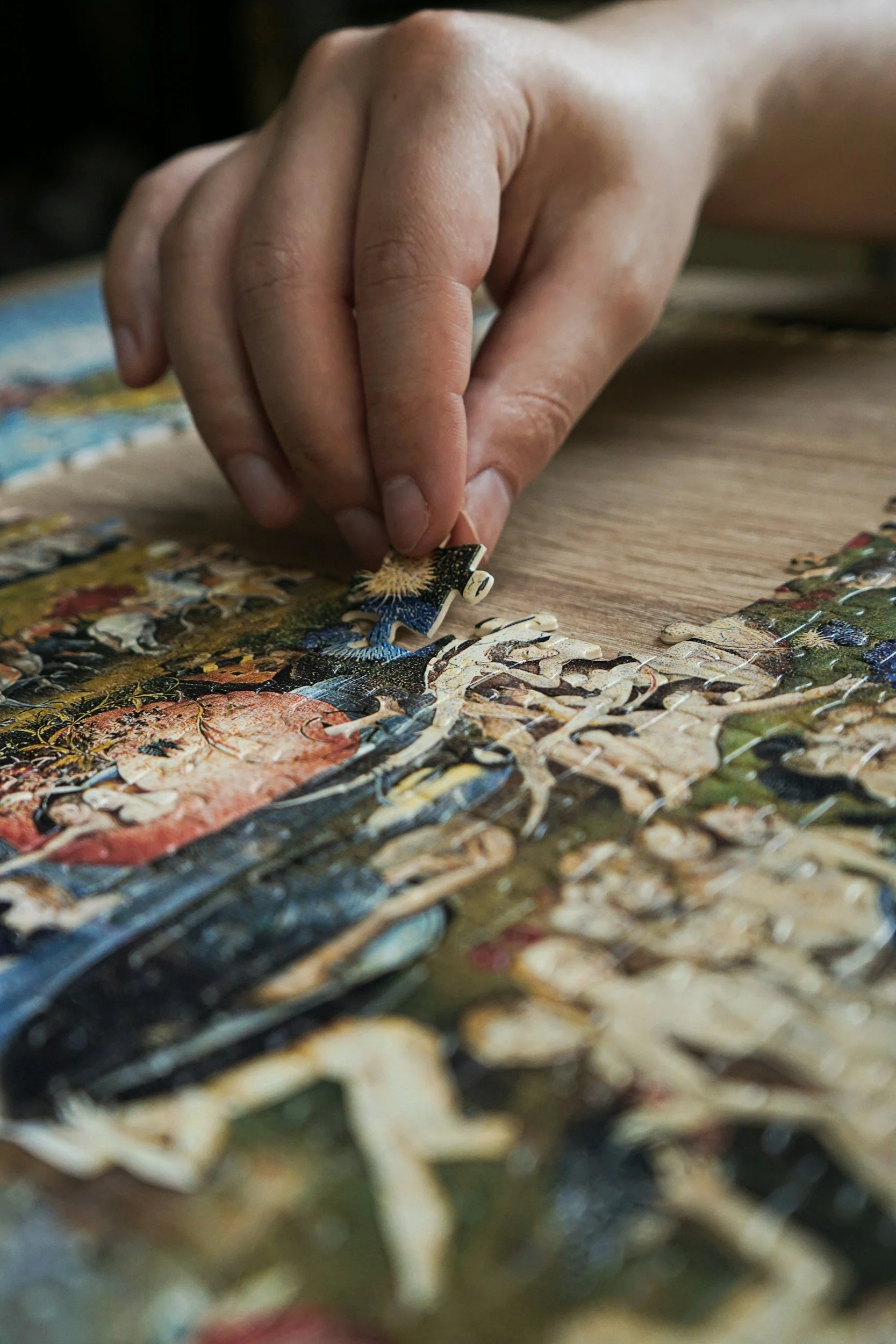 Close-up of a hand placing a puzzle piece into a colorful jigsaw puzzle on a wooden surface.