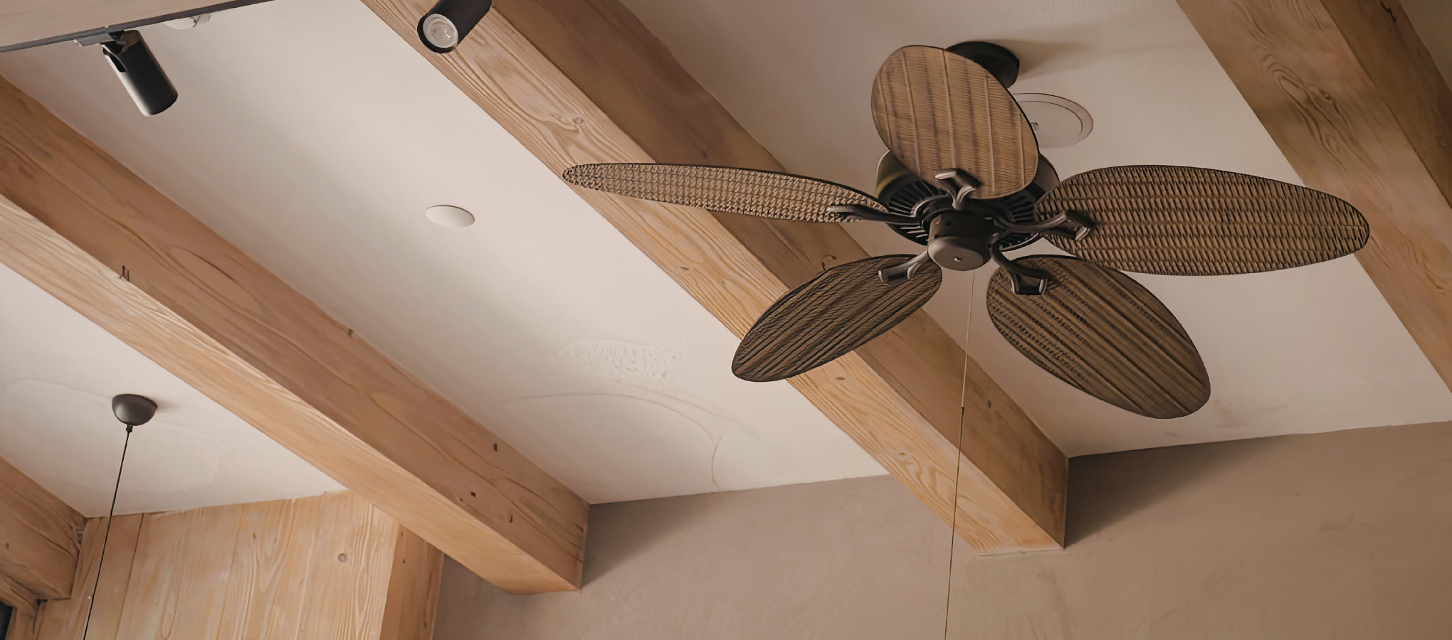Wood-paneled ceiling with a ceiling fan featuring five wooden blades and black fixtures, along with black track lighting.