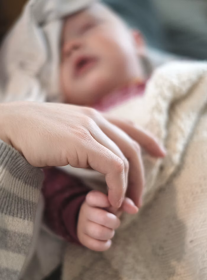 A close-up of a child's hand holding an adult's finger, with the child's face blurred in the background.