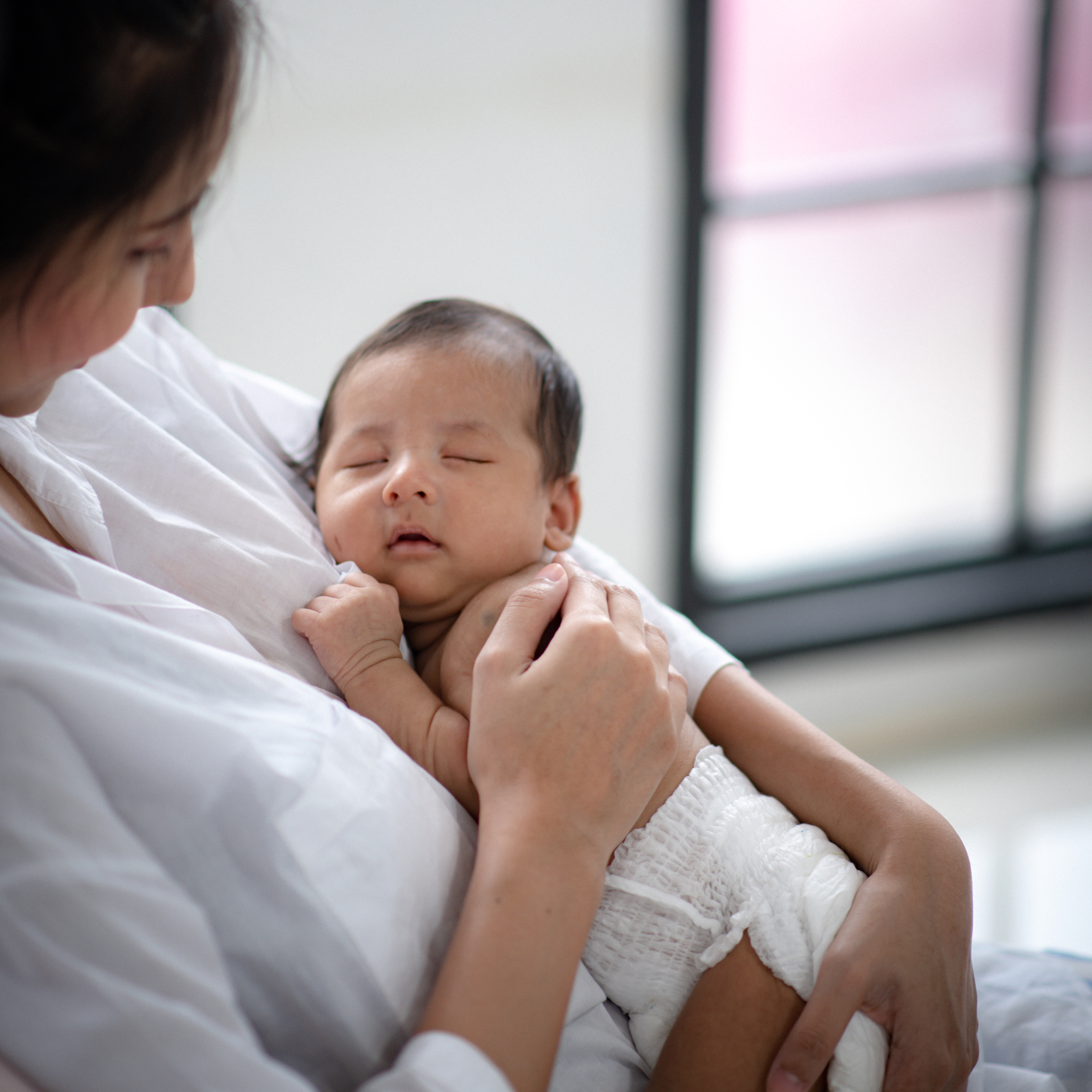 A person holding a sleeping child close in a hospital or medical setting, both wearing white clothing.