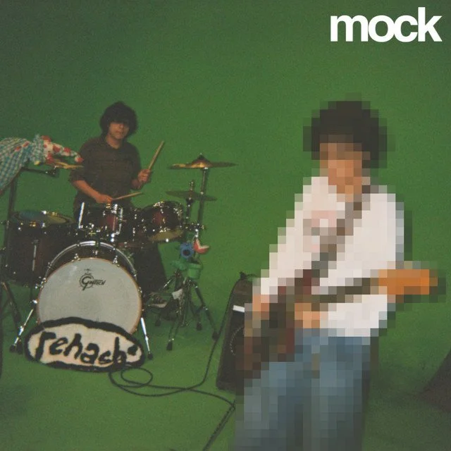 Two guys playing musical instruments in front of a green screen. One is standing behind a drum set, and the other is holding an electric guitar. The background is a solid green color.