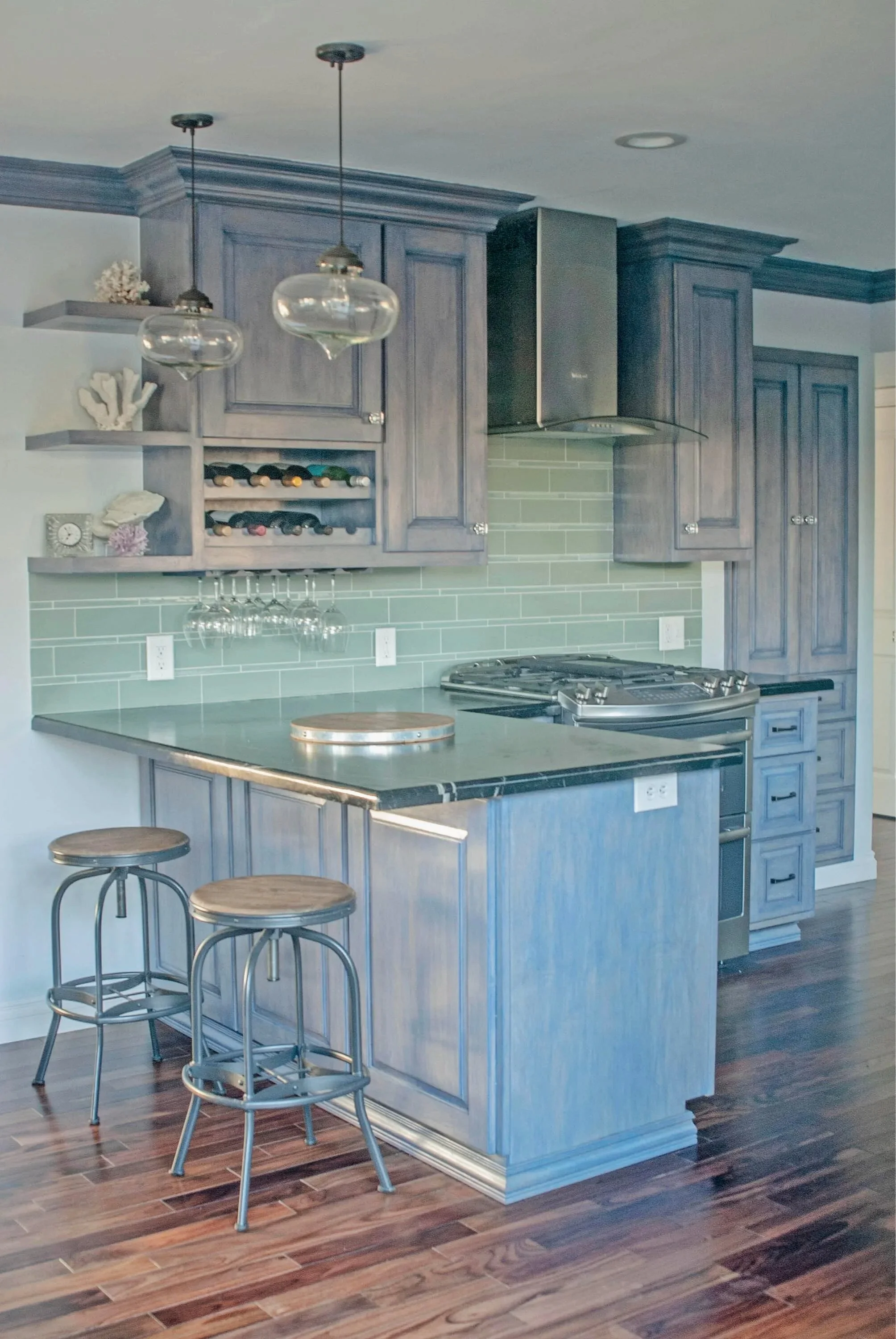 Modern kitchen with blue cabinetry, a kitchen island with stools, pendant lights, green subway tile backsplash, and wooden flooring.
