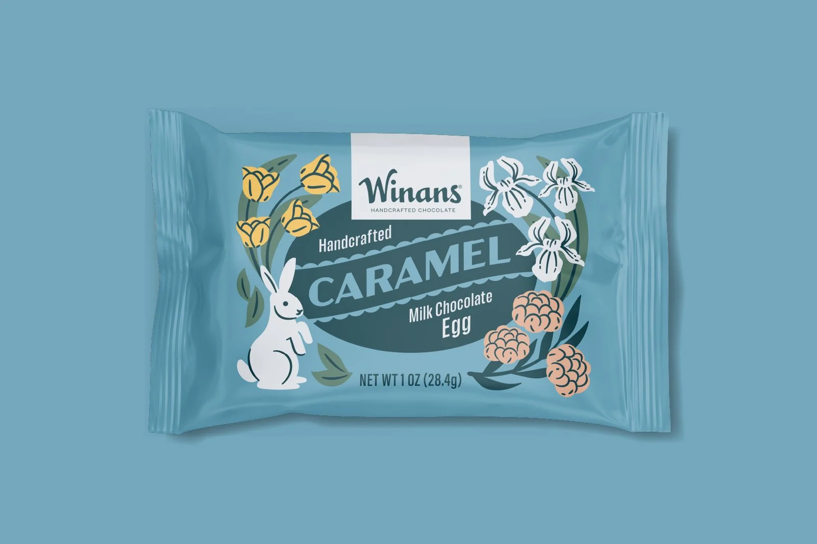 A blue package of Winans handcrafted caramel milk chocolate egg with floral illustrations and a playful bunny character on the front. Packaging design and illustration by Slagle Design. 