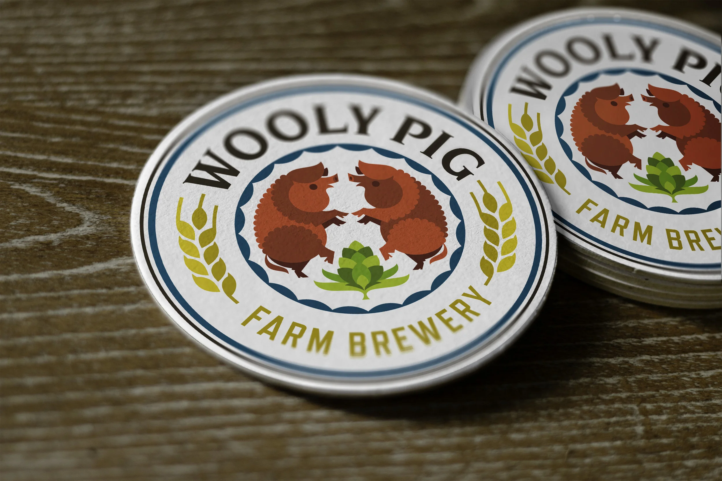 Close-up of round coasters with logo featuring two red hedgehogs, wheat stalks, and the text 'Wooly Pig Farm Brewery' on a wooden surface.