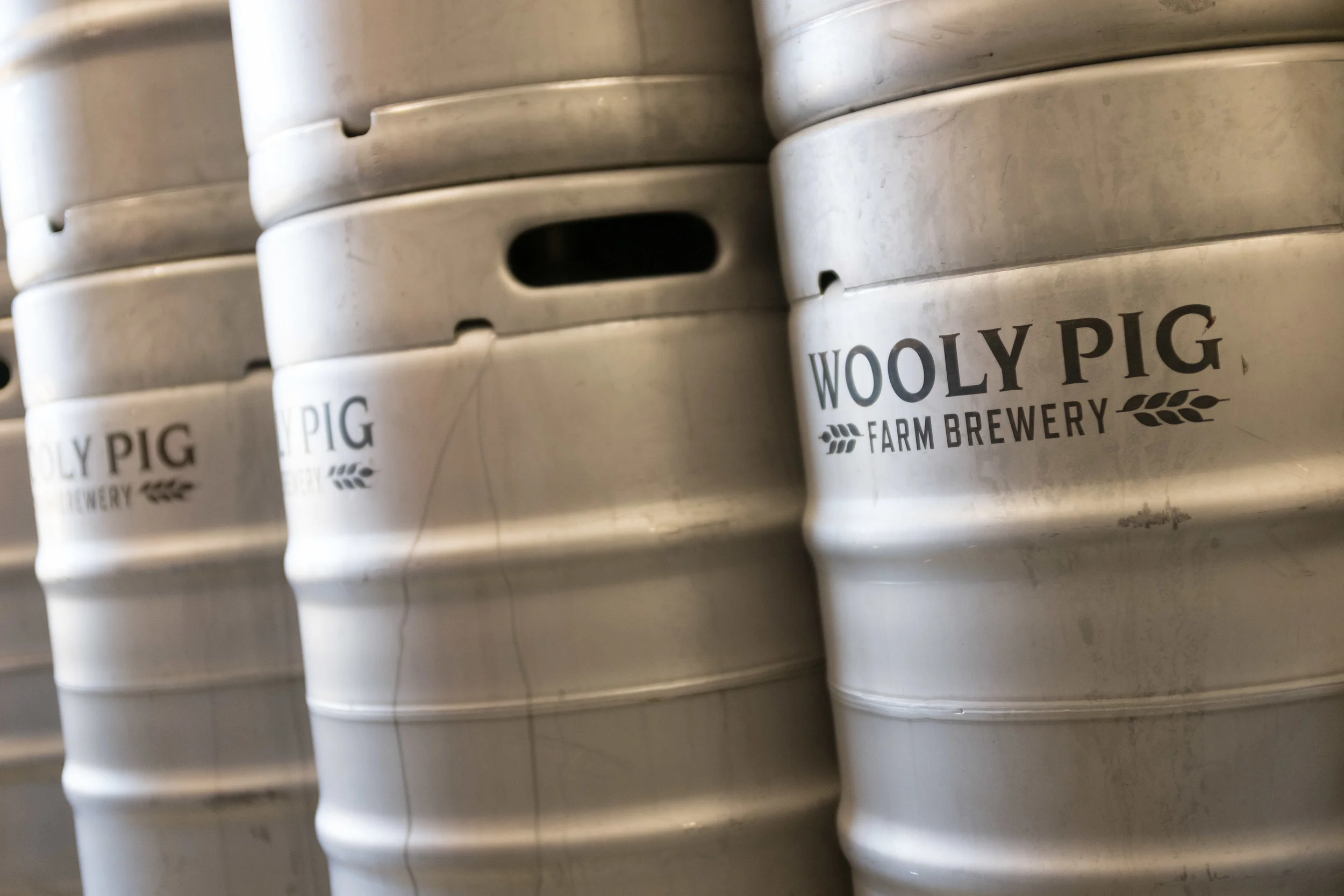Stacks of metal beer kegs with the label 'Wooly Pig Farm Brewery' printed on them.