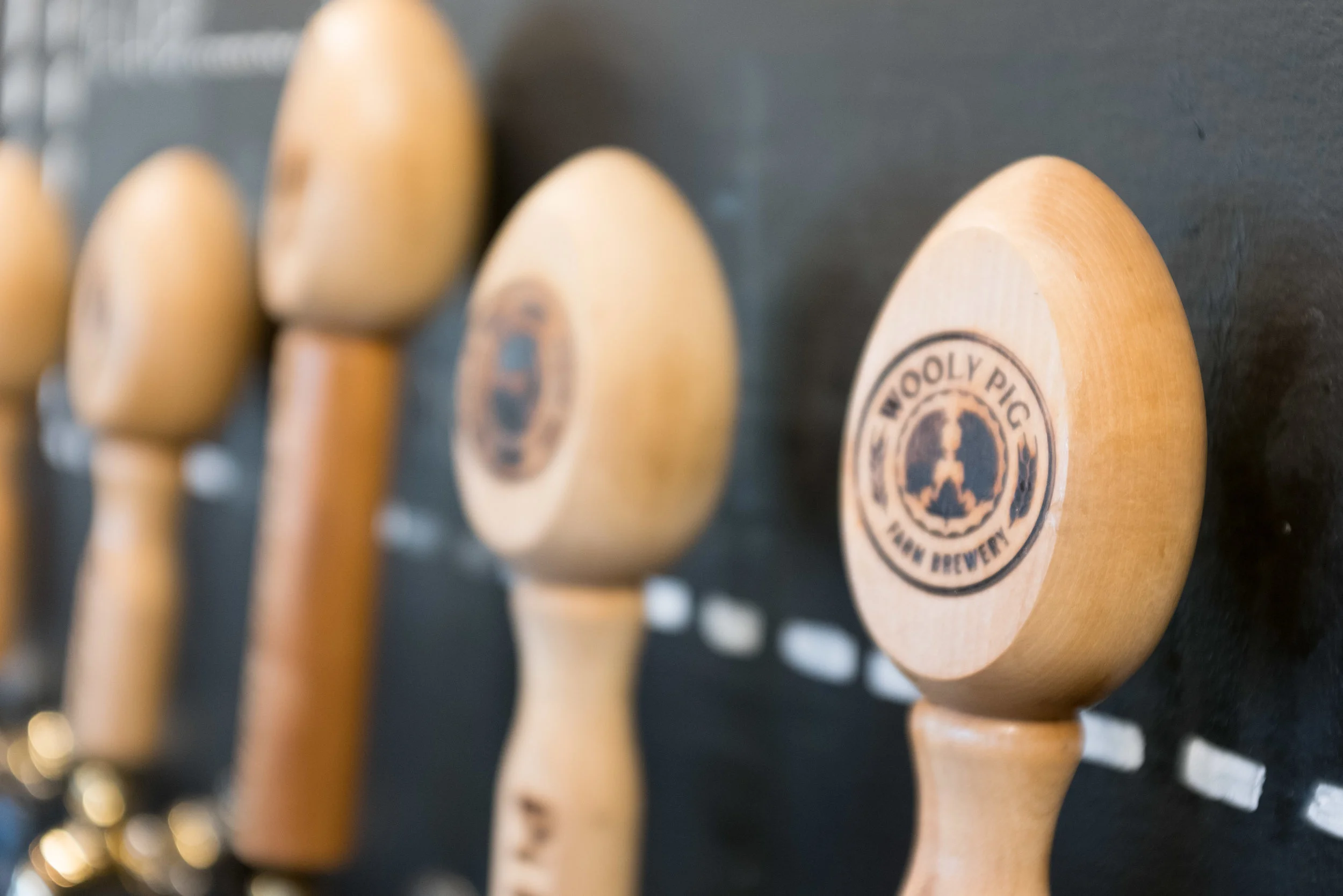 Close-up of beer tap handles, one with an engraved logo reading 'Wooly Pig' and 'New Brewery' in black ink.