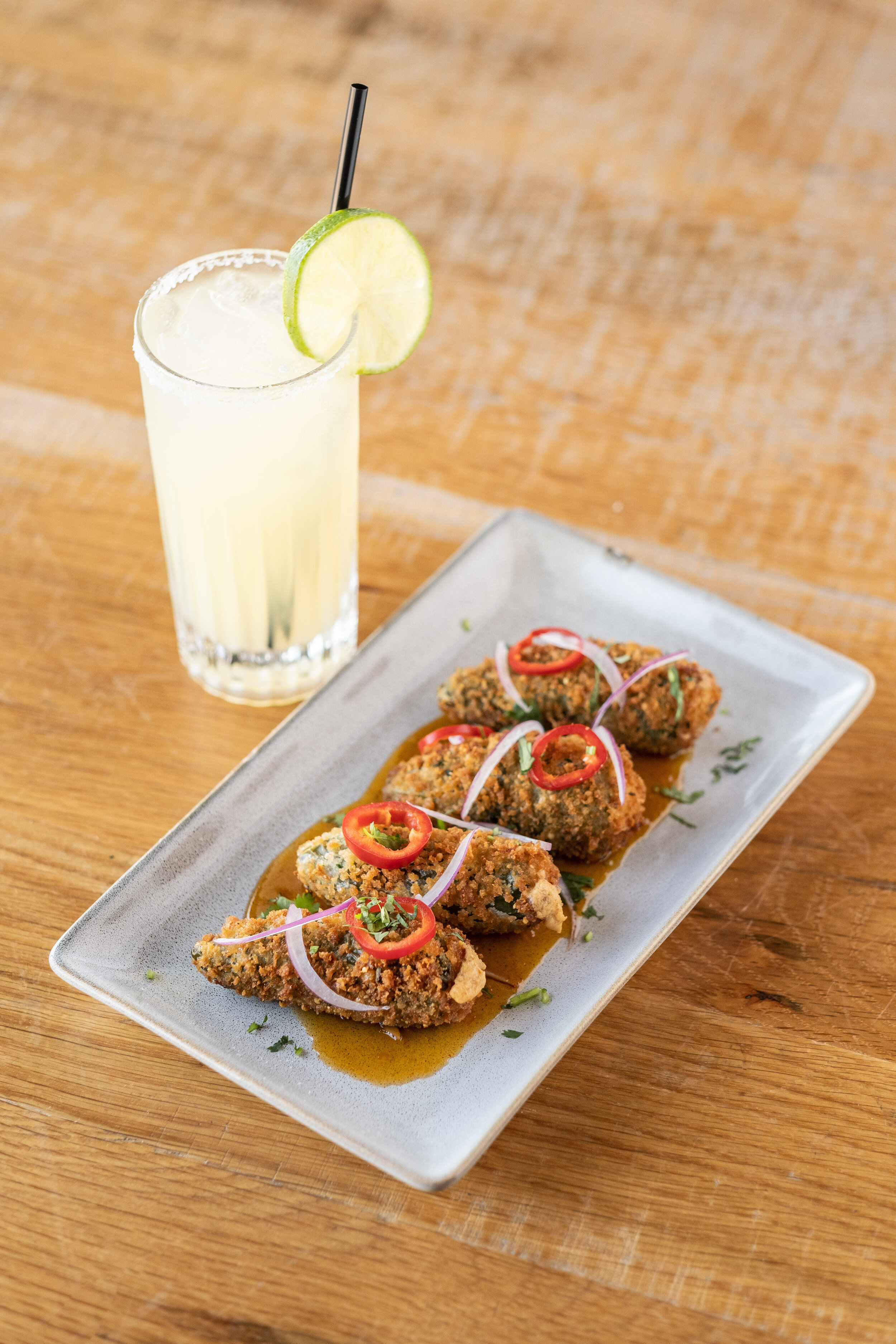 Fried appetizers garnished with sliced red chilies and onions served with a lime drink on a wooden table.
