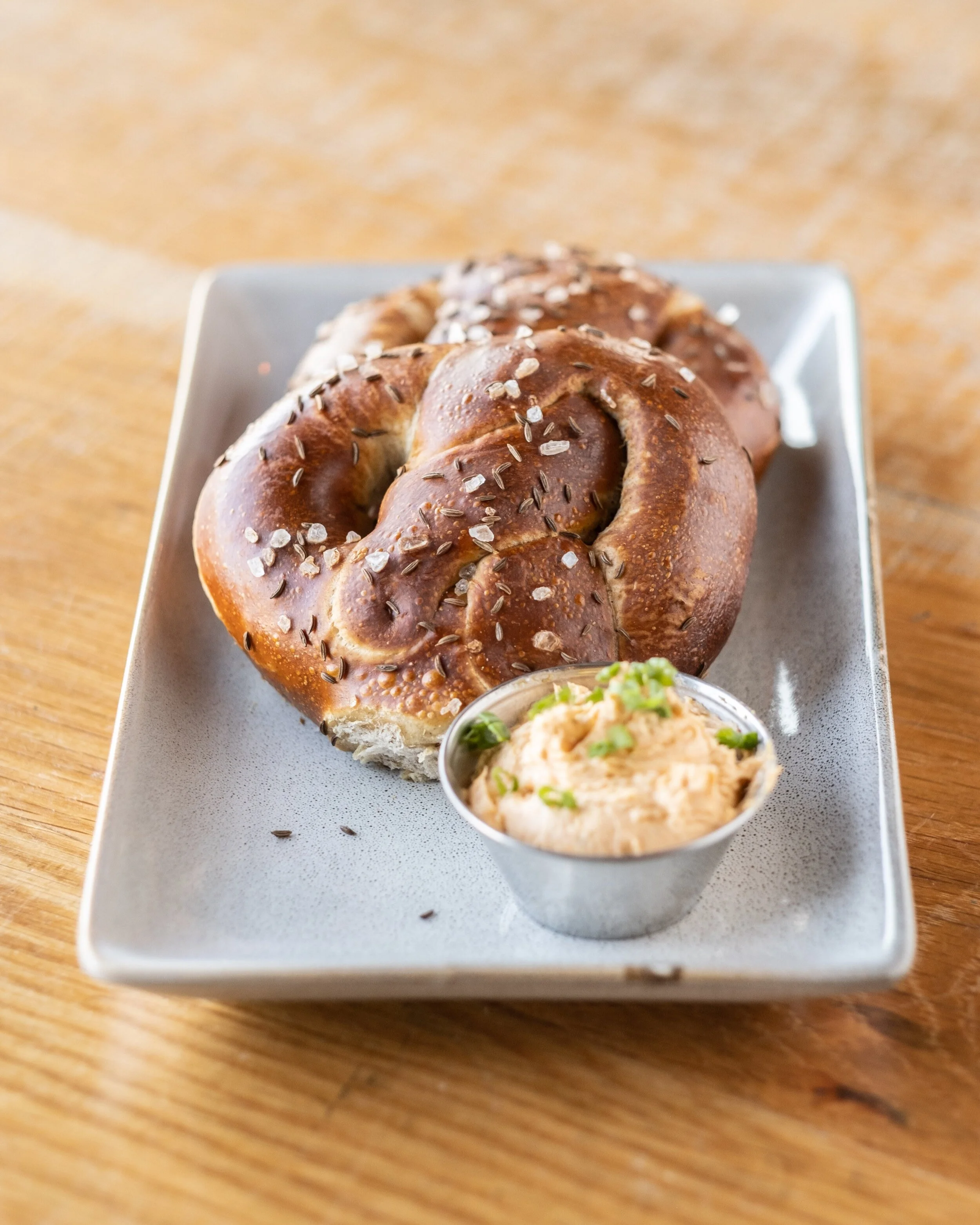 A pretzel with coarse salt and caraway seeds served with a side of spicy mustard on a square gray plate.