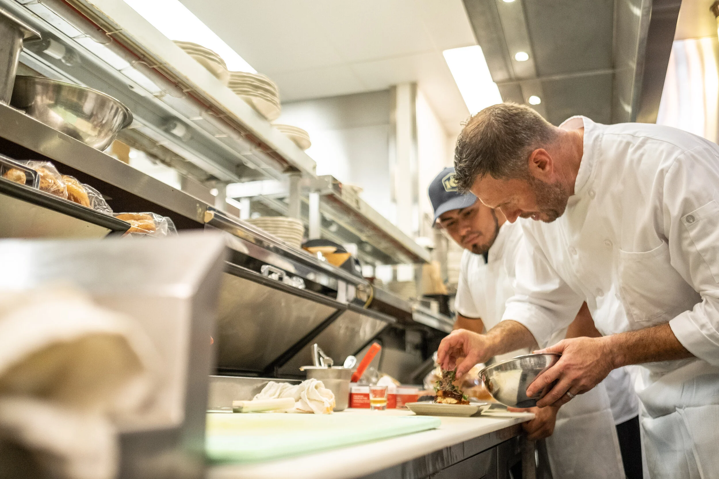 Chefs preparing food in a professional kitchen, focusing on plating a dish.