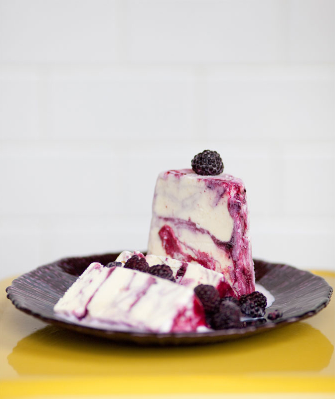 Slices of blackberry cheesecake with fresh blackberries on a black plate.