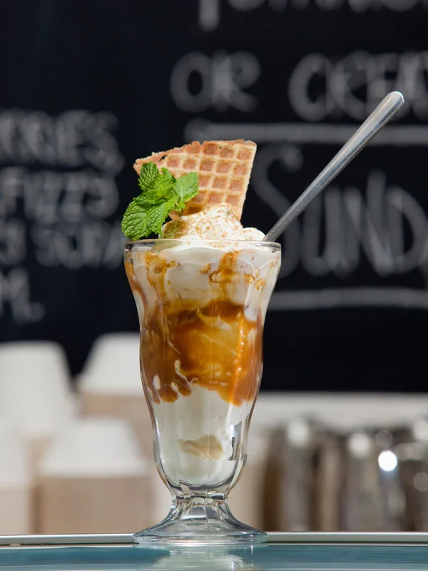 Ice cream sundae with caramel drizzle, a waffle cone piece, and mint garnish in a tall glass