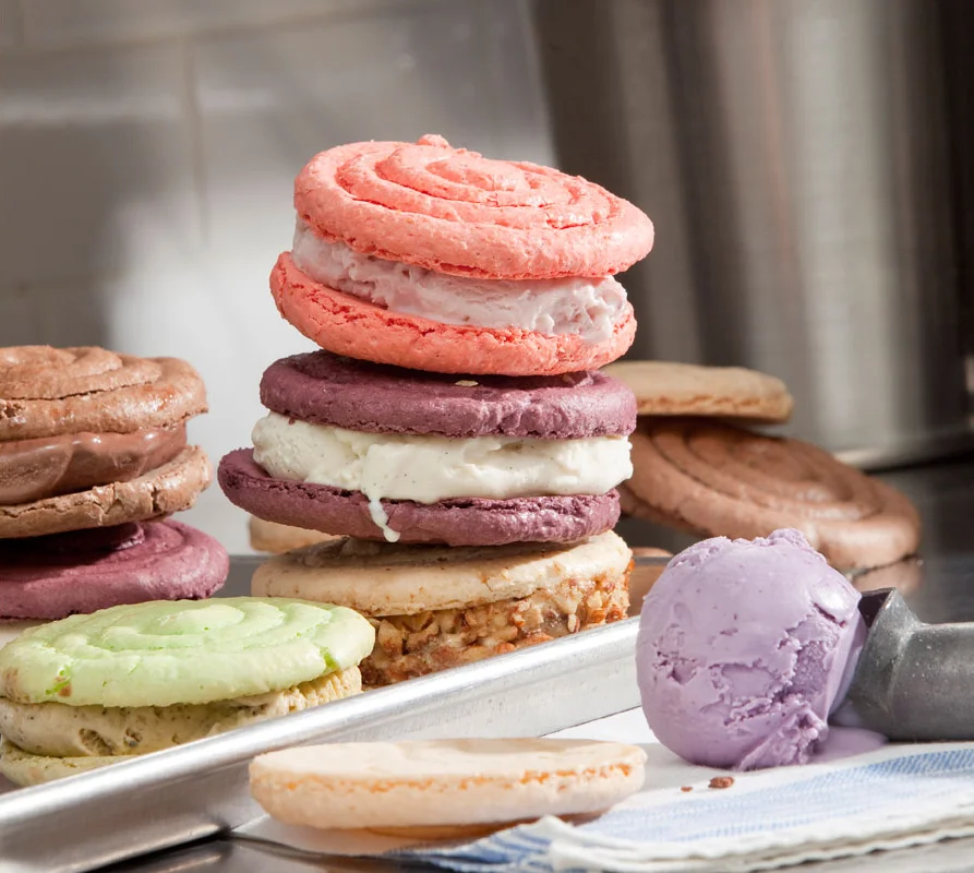 Stacked colorful macarons on a metal tray, with some macarons and ice cream scoops nearby.