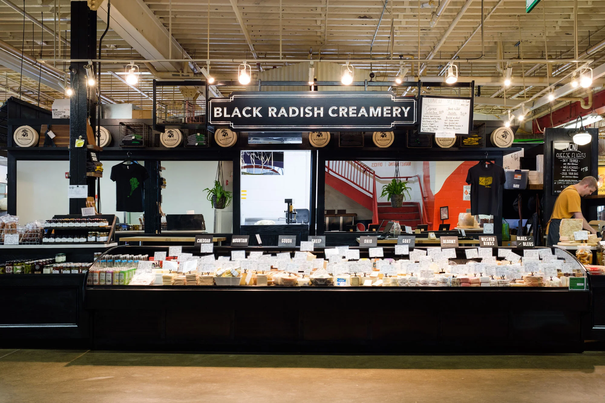 Cheese shop named Black Radish Creamery with various cheeses on display and a person working behind the counter.