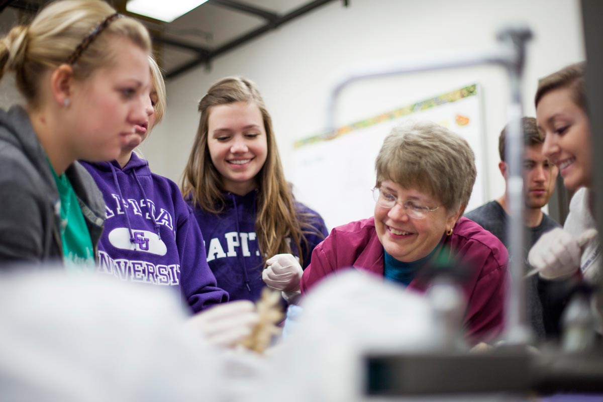 A group of students and a woman in a lab, smiling and working together on a project.
