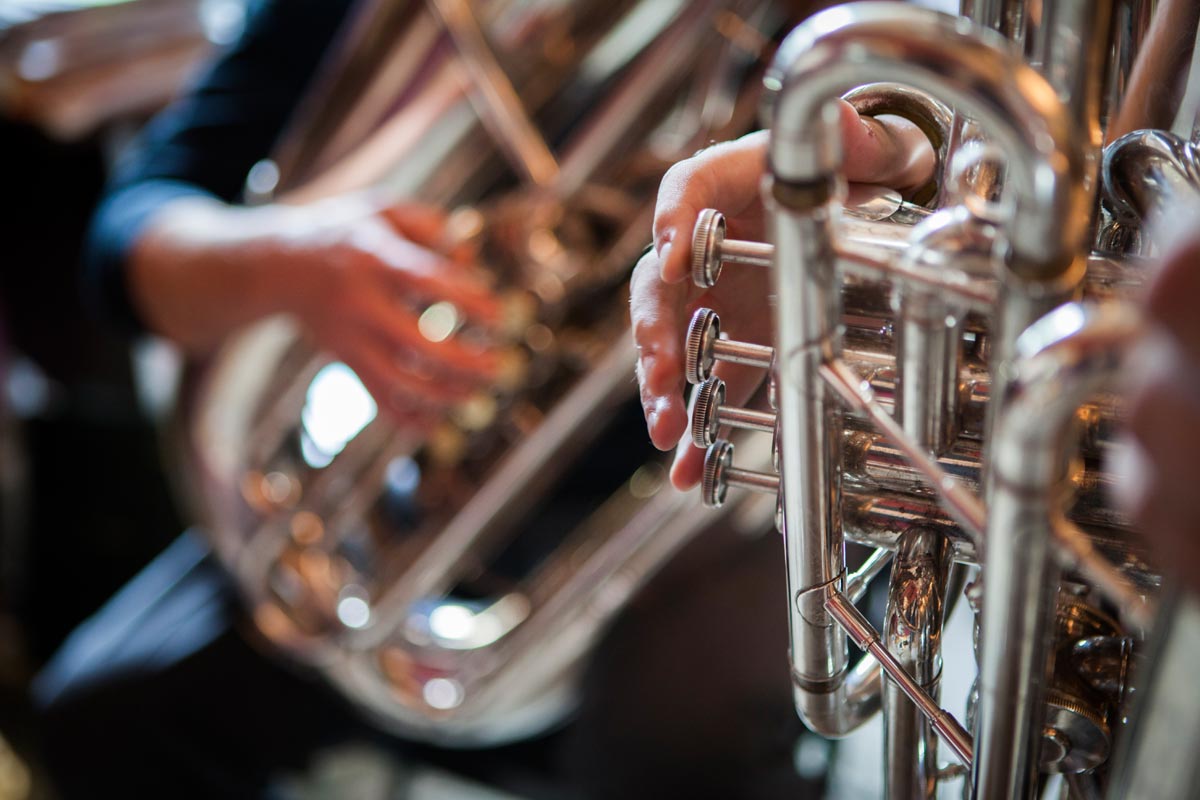 Close-up of a person's hand adjusting the valves of a silver trumpet.