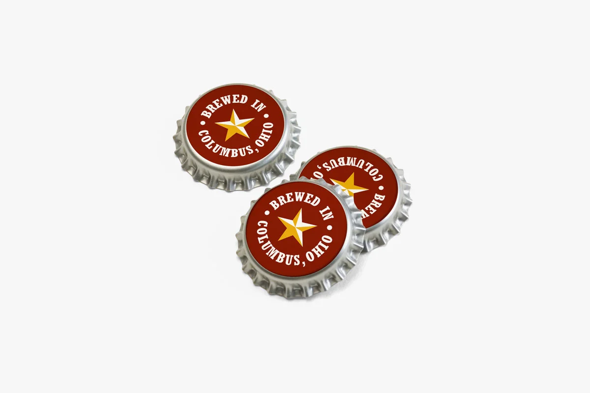 Three bottle caps with the text 'Brewed in Columbus, Ohio' and a star symbol on a plain white background.