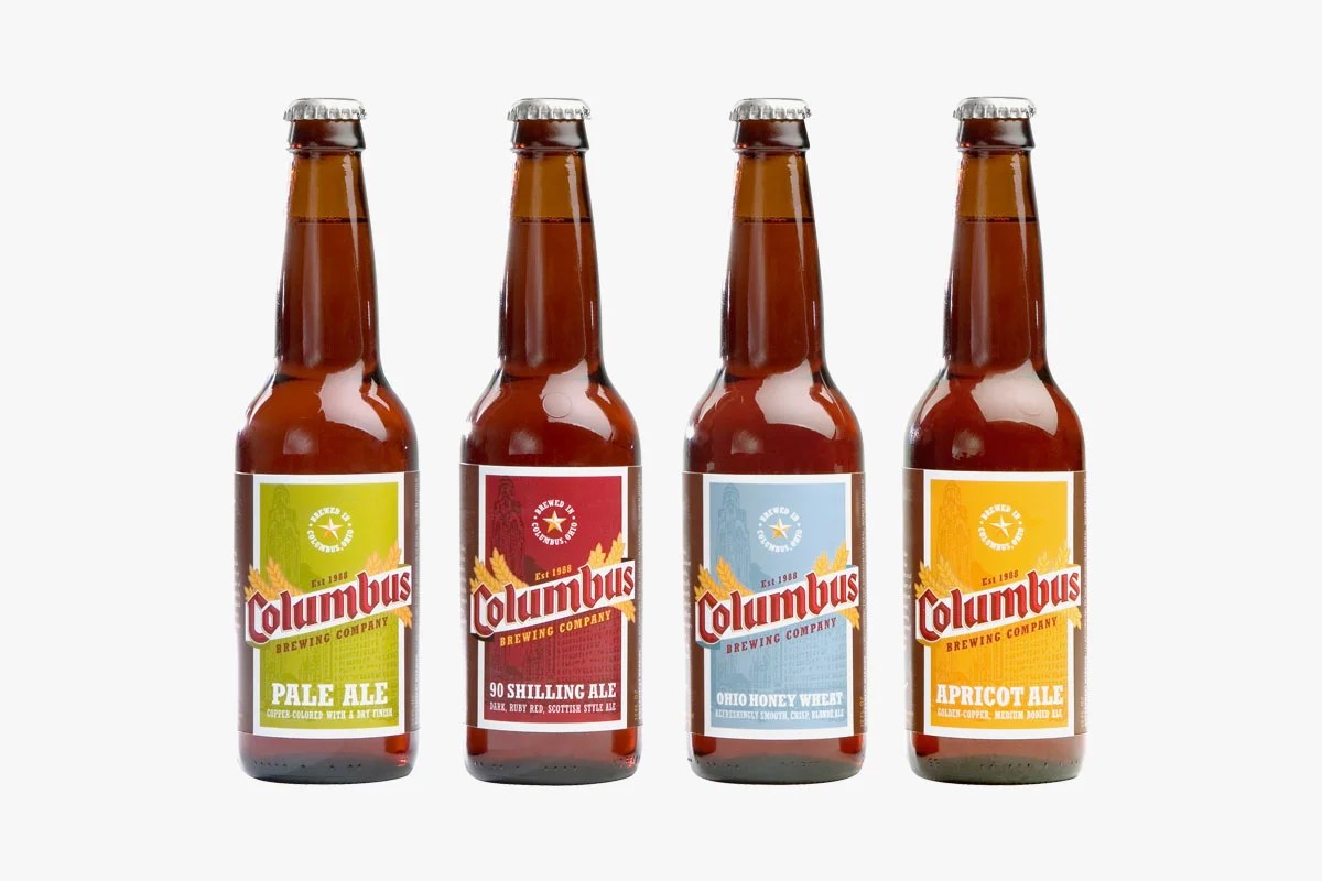 Four bottles of Columbus Brewing Company craft beers line up on a white background, each with colorful labels: Pale Ale, 90 Shilling Ale, Ohio Honey Wheat, and Apricot Ale.