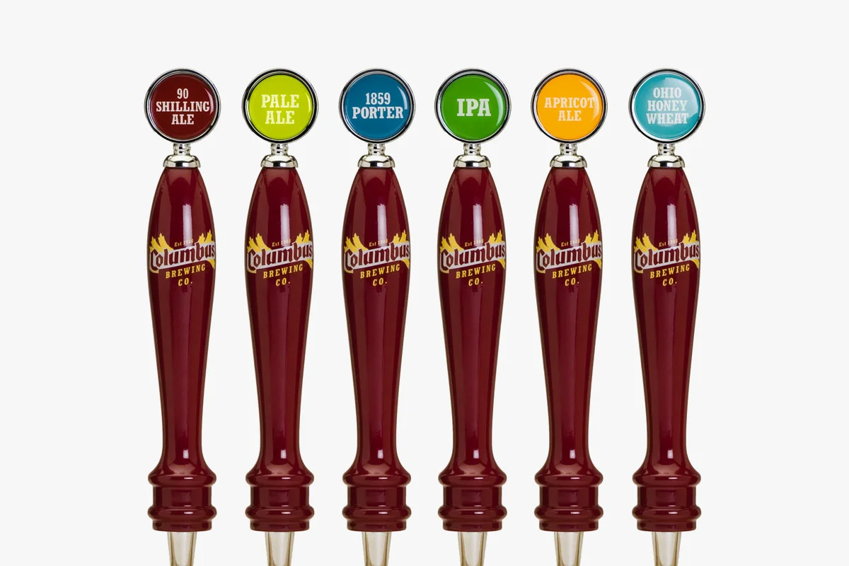 Six beer taps with Columbus Brewing Co. logo, labeled from left to right: 90 Shilling Ale, Pale Ale, 1859 Porter, IPA, Apricot Ale, Ohio Honey Wheat.