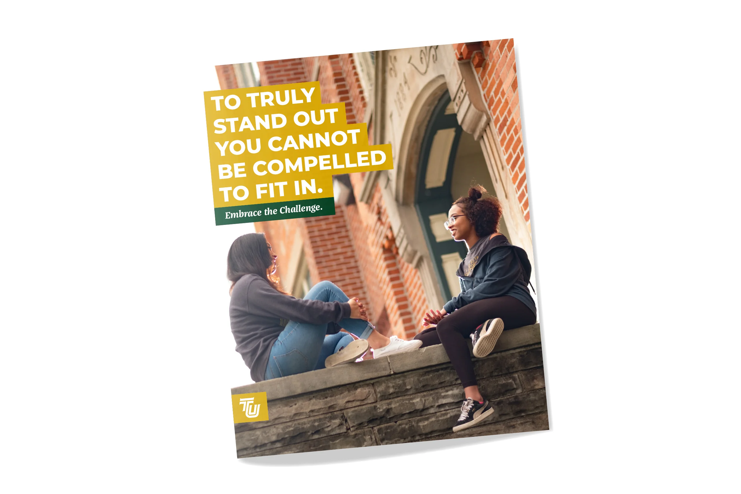 Two young women sitting on a stone ledge engaging in conversation outside a brick building with green door and arched windows, smiling and facing each other.