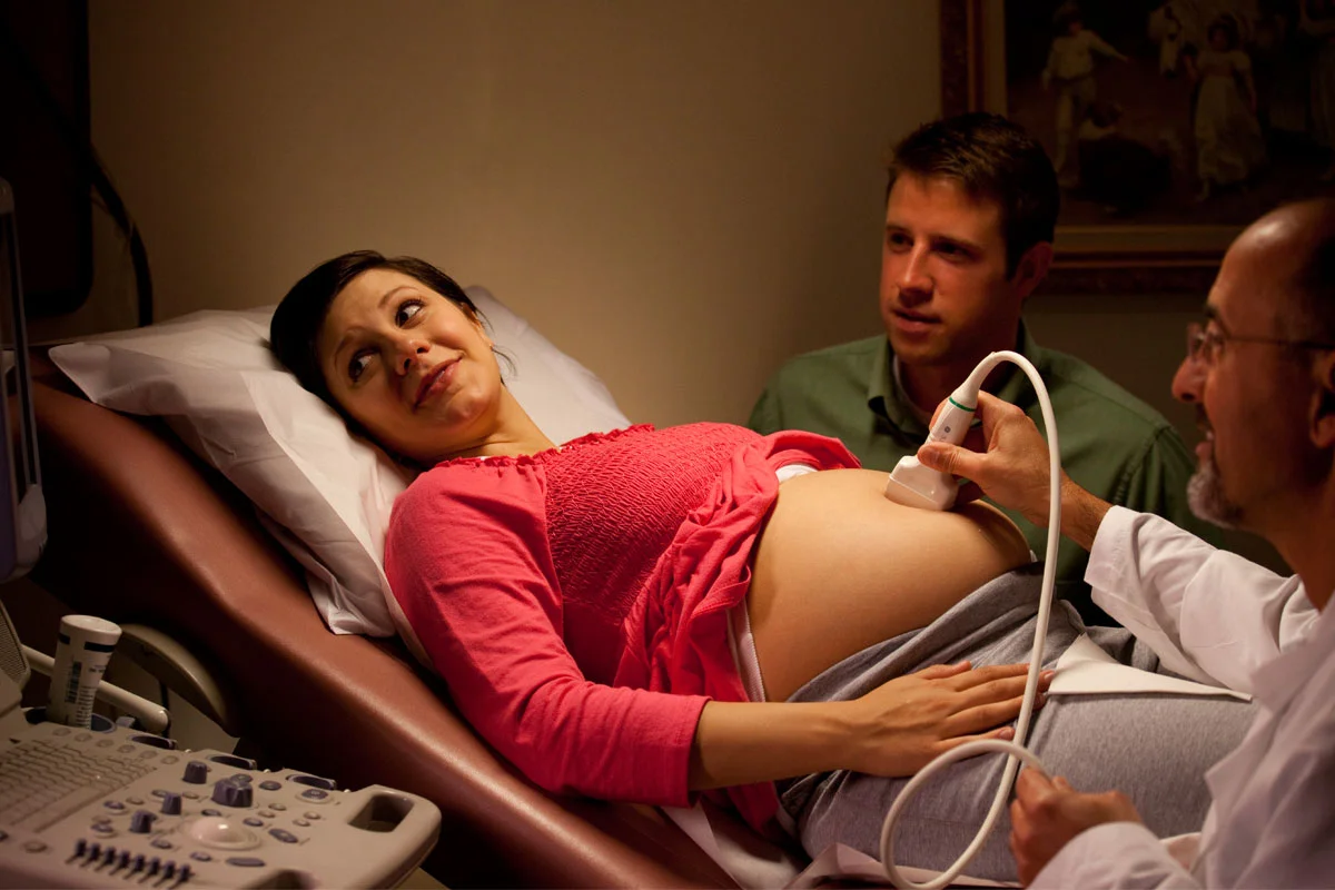 A pregnant woman lying on an examination table during an ultrasound with her partner and a medical professional present.