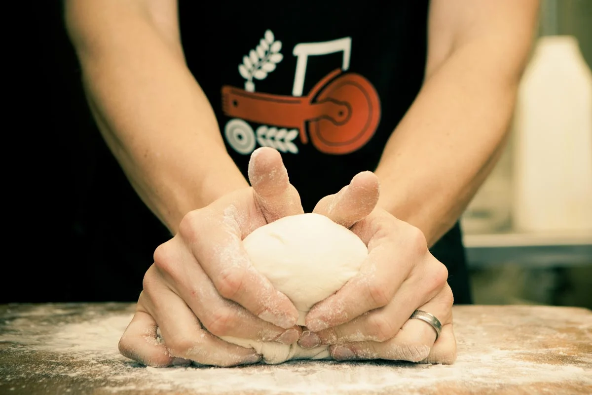 Person kneading dough on a floured surface in a kitchen.
