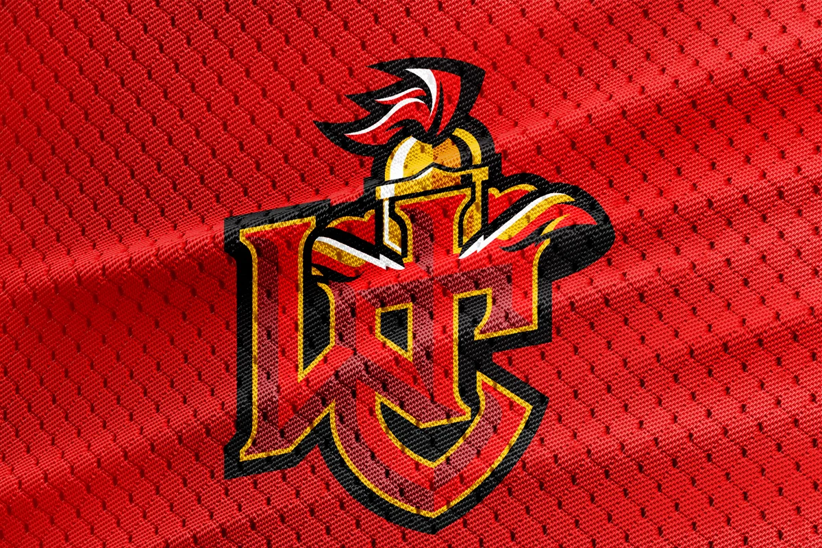 Close-up of a red sports jersey with a logo of a stylized Trojan head and a shield, featuring the letters 'U' and 'T' intertwined, outlined in black with yellow accents.