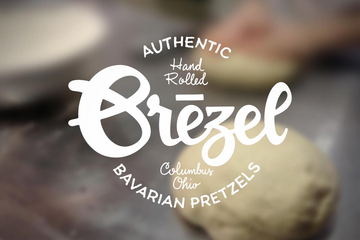 Close-up of a pretzel with a logo overlay reading 'Authentic Hand Rolled Biezl', with additional text 'Columbus Ohio' and 'Bavarian Pretzels'.