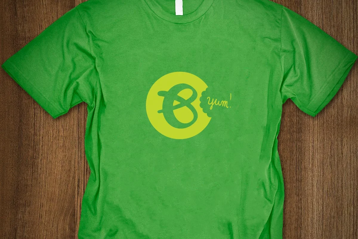 Green T-shirt with a yellow cartoon smiley face and speech bubble, with the word 'yum!' written inside the bubble.