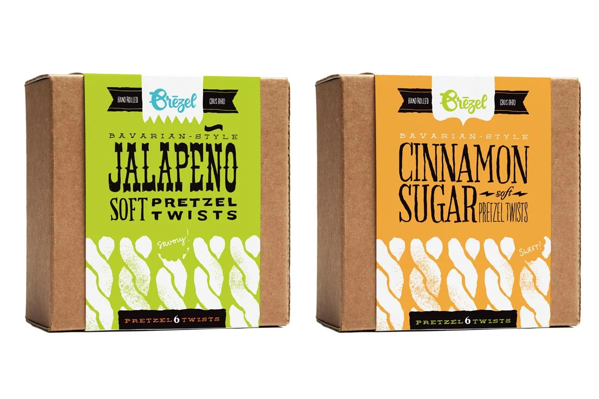 Two boxes of Bavarian-style pretzel twists, one with jalapeno flavor and the other with cinnamon sugar flavor, both hand rolled from Ohio. The jalapeno box is green and the cinnamon sugar box is orange.