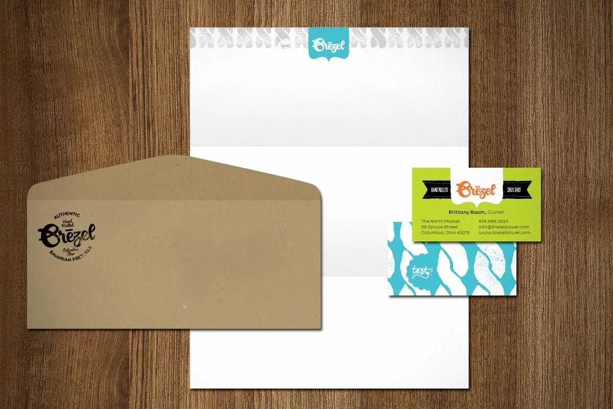 Business card, envelope, and letterhead for Brezel, a Bavarian pretzel company, displayed on a wooden surface.